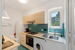 A compact kitchen with a built-in washing machine, a window with a view, and a sink. - Apartment 'Annabella' with Sea View, Wi-Fi and Air Conditioning (Sorrento)