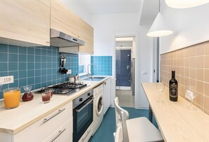 Une cuisine moderne équipée d’une cuisinière à gaz, d’un four, d’un lave-linge et d’un évier. On peut voir deux verres à vin et une bouteille sur le plan de travail.