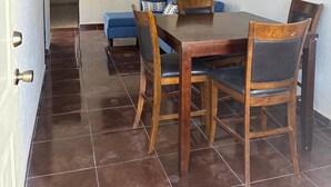 Ein Essbereich mit Holztisch und Stühlen, einem blauen Sofa und einem an der Wand befestigten Flachbildfernseher.