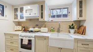A kitchen with a gas stove, oven, microwave, and a sink. There are cabinets above the counter and a window above the sink.