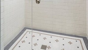 A glass-enclosed shower with white subway tiles and a patterned floor.