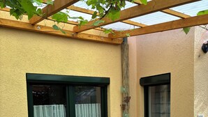 A glass table with chairs, a window with a curtain, and a wooden pergola structure.