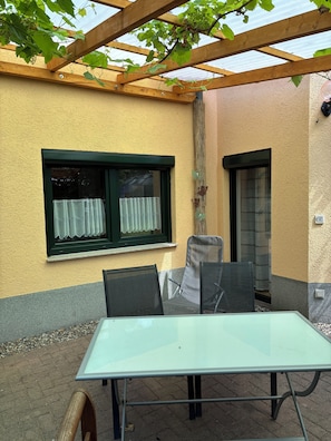 Ein Glastisch mit Stühlen, ein Fenster mit Vorhang und eine Holzw pergola.