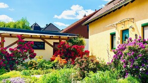 A yellow building with a tiled roof, a wooden pergola, and a variety of colorful flowers in the garden.