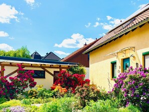 A yellow building with a tiled roof, a wooden pergola, and a variety of colorful flowers in the garden. - Enjoy a vacation on the edge of Saxon Switzerland (Dürrröhrsdorf-Dittersbach)