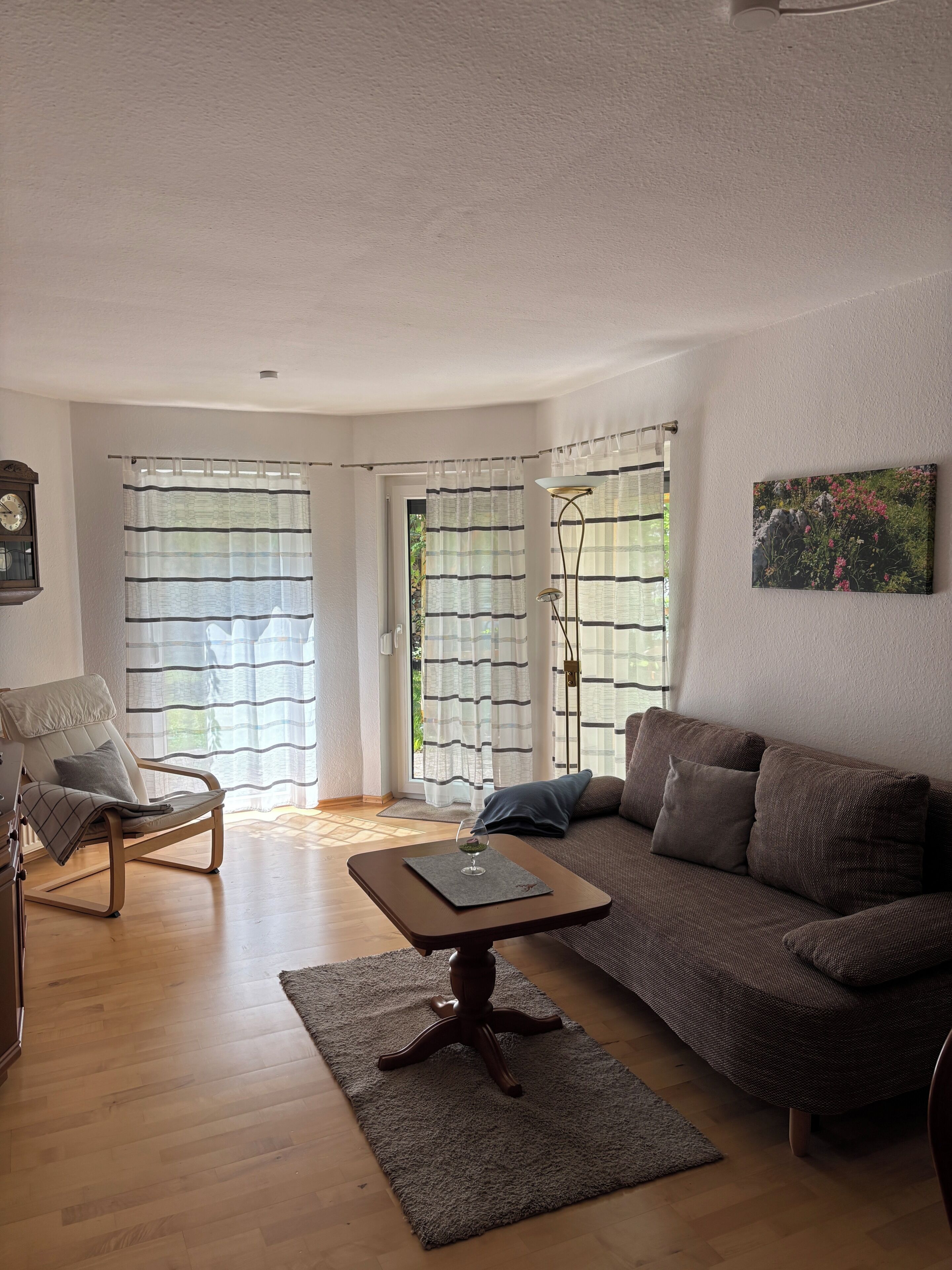 Ein Wohnzimmer mit einer Couch, einem Sessel, einem Holztisch und einer Stehlampe.