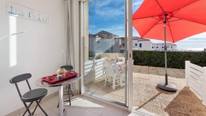 Een balkon met een tafel, stoelen en een rode parasol.