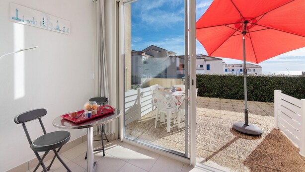 Un balcon avec une table, des chaises et un parasol rouge.