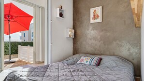 Een slaapkamer met een bed, een rode paraplu buiten en een uitzicht op gebouwen.