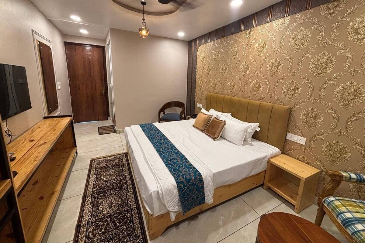 A bedroom with a bed, bedside tables, a wooden bench, a TV, and a patterned wall.