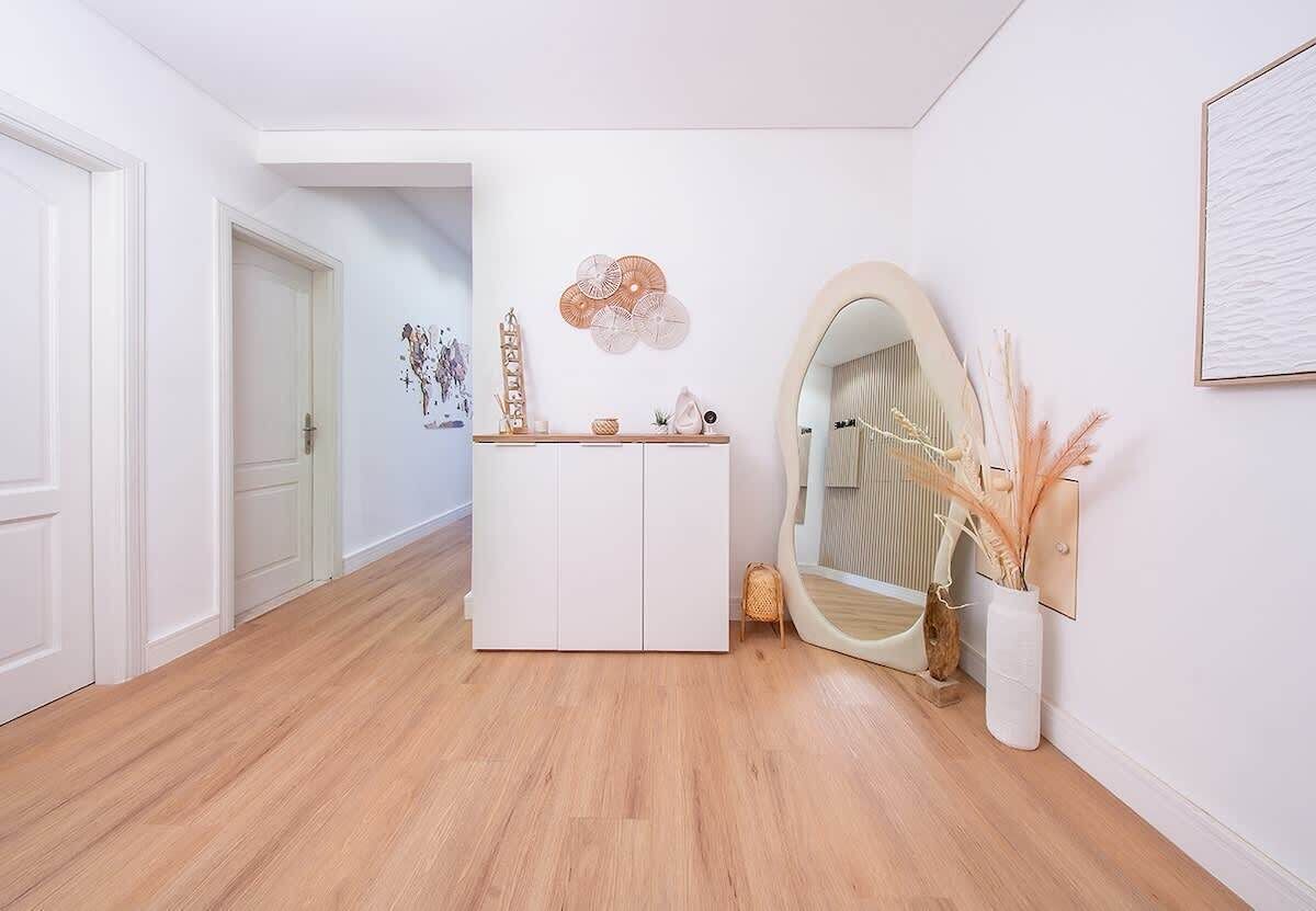A hallway with a white door, a white cabinet, a mirror, and a wall-mounted decorative piece.