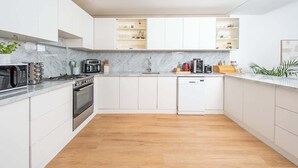 A modern kitchen with white cabinetry, a built-in oven, a dishwasher, and a marble countertop.