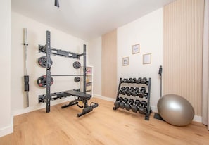 A compact home gym with a squat rack, bench, weight plates, a rack of dumbbells, and an exercise ball. - Al Furjan Villa WPrivate Pool & Gym Near Marina (Dubai)