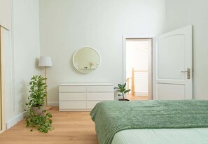 Een slaapkamer met een bed, een kapstok, een spiegel en een deur.
