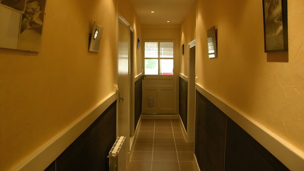 A hallway with a radiator, framed pictures, and a door at the end. - Historic Post House Gîte, 8 Bedrooms (Les Rousses)
