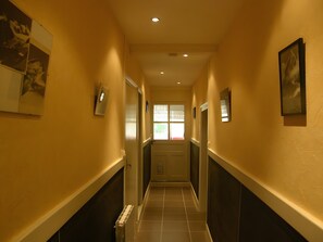 A hallway with a radiator, framed pictures, and a door at the end. - Historic Post House Gîte, 8 Bedrooms (Les Rousses)