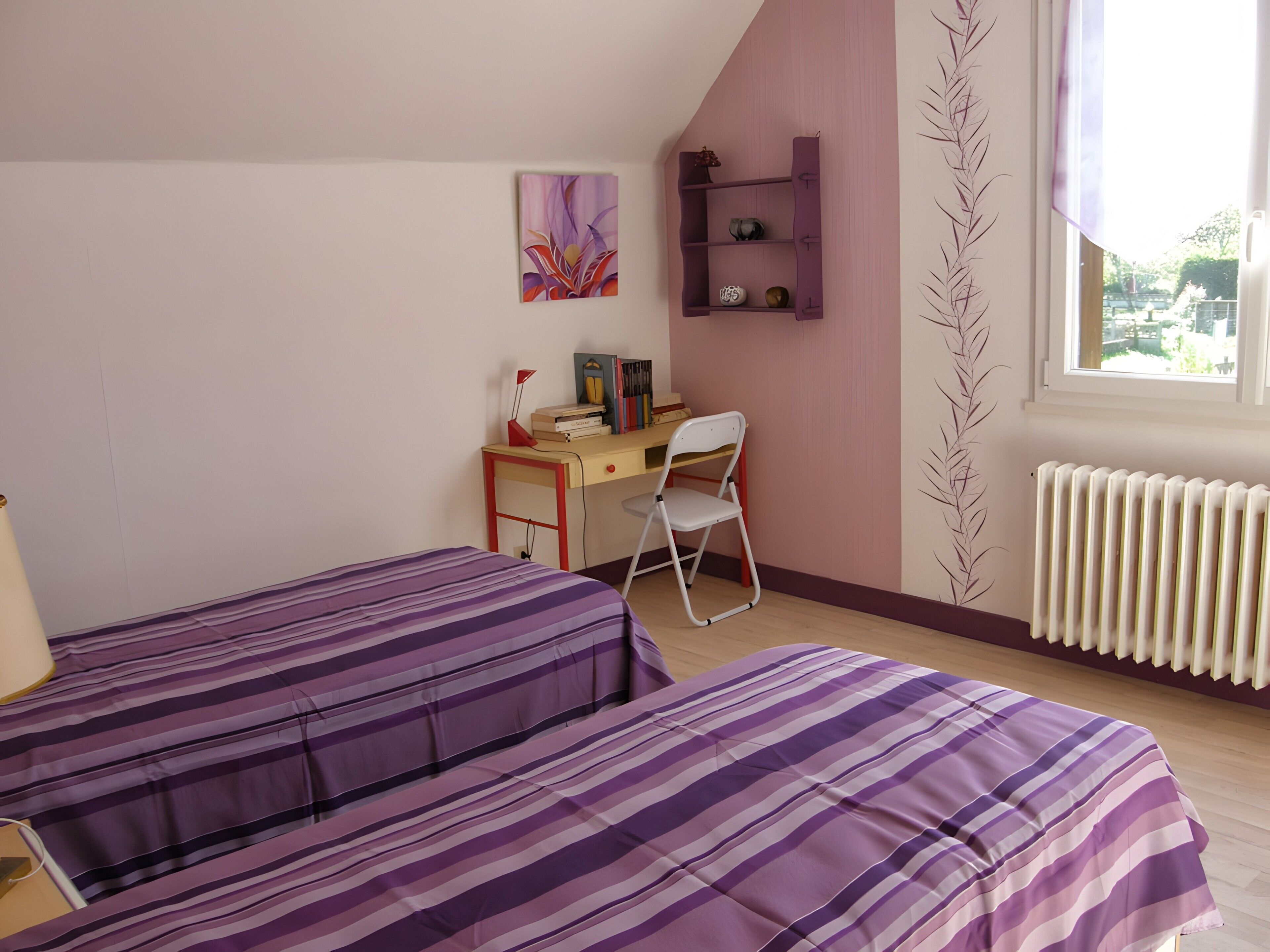 Ein Schlafzimmer mit zwei Betten, einem Schreibtisch, einem Stuhl, einem Heizkörper und einem Fenster.