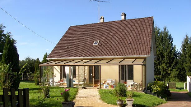 Una casa de dues plantes amb teulada de rajola, un porxo cobert i un jardí davanter amb plantes en testos.
