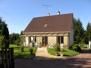 A two-story house with a tiled roof, a covered porch, and a front yard with potted plants.