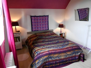 A bedroom with a bed, a nightstand, a lamp, a radiator, and a window with curtains. - Country House for 7 People (Guérigny)