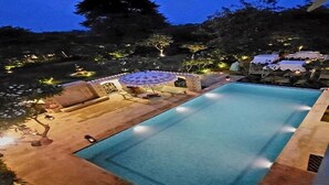 A swimming pool with a sun lounger and umbrella, surrounded by trees and outdoor lighting. - Bhanpur Haveli | Hidden Luxury Haveli Amid Greenery & Peace (Jamwa Ramgarh)