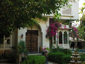 Un edificio tradicional con una puerta de madera grande, ventanas arqueadas y una fuente en el jardín.