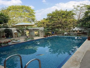 Una piscina con borde de azulejos, rodeada de plantas en macetas y una pérgola.