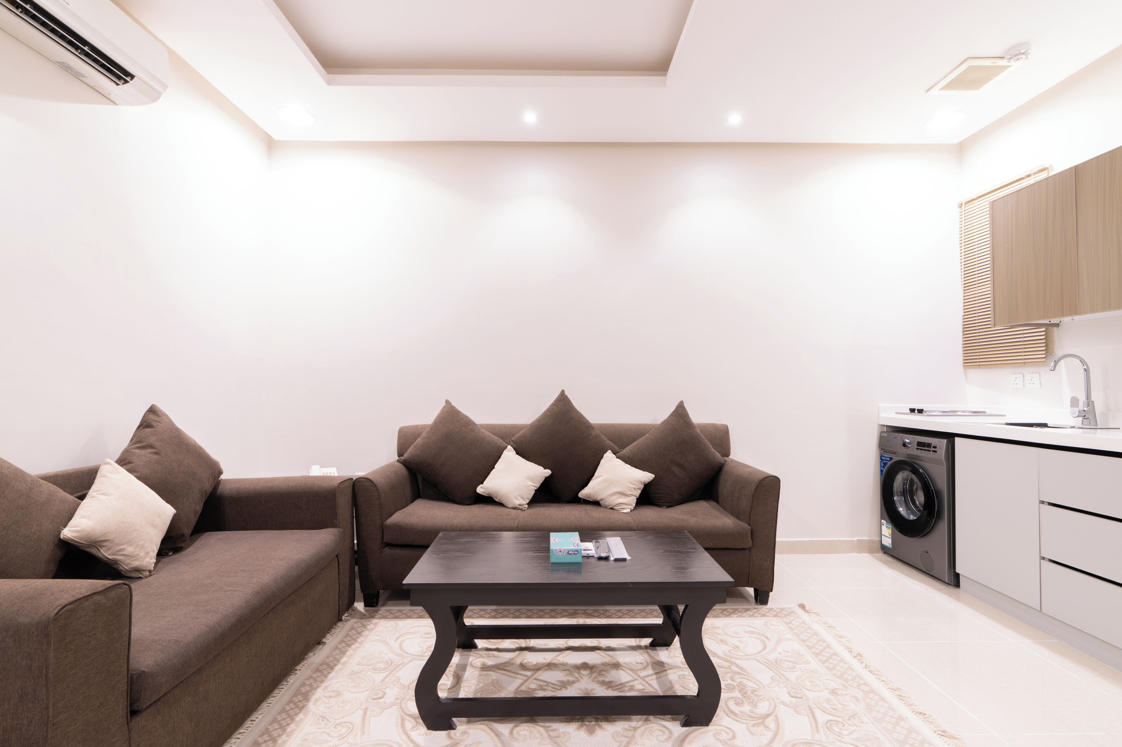 A modern living room with a sofa set, a coffee table, and a washing machine in the corner.