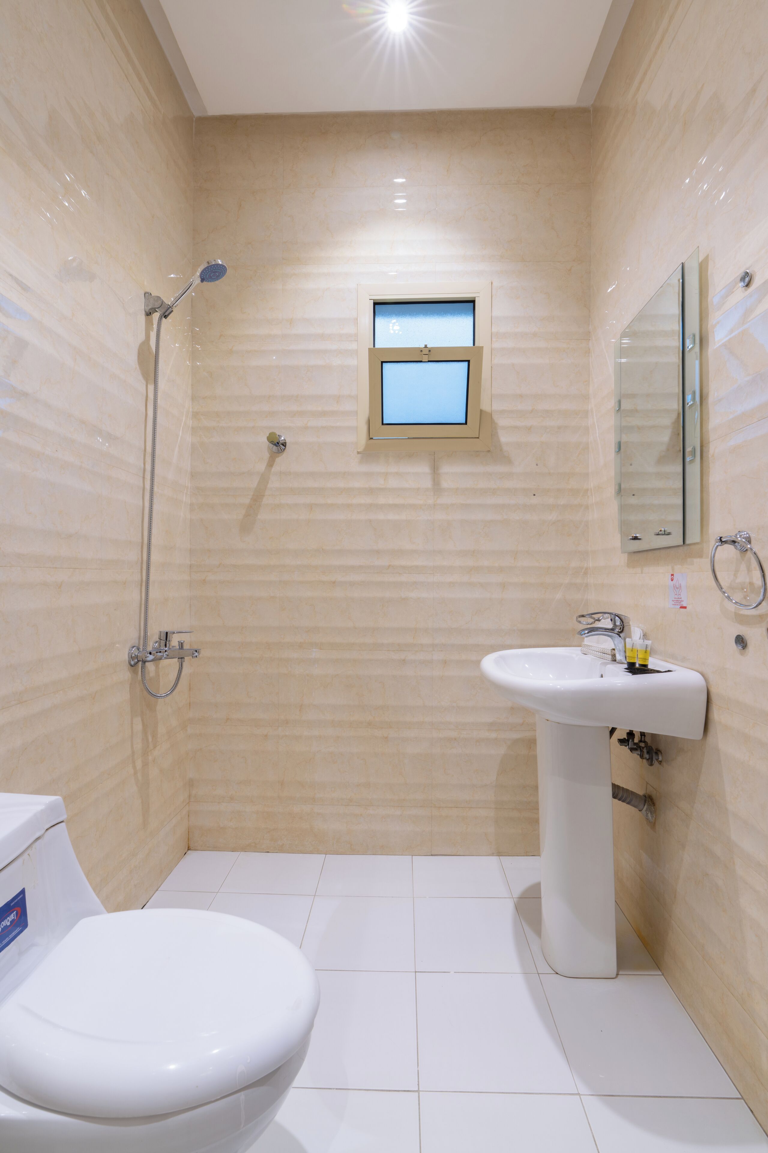 A bathroom with a toilet, sink, shower, and a small window.