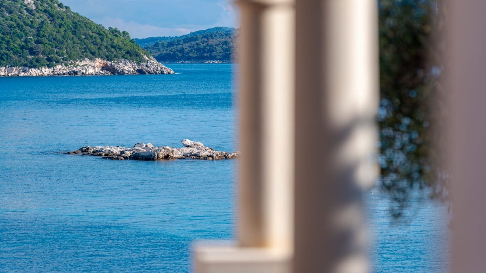 A coastal view with a rocky outcrop in the water, surrounded by hills and clear skies.