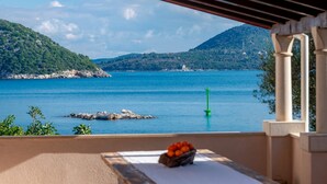 Ein Balkon mit Blick auf ein ruhiges Meer, ein grüner Boje und eine Schale Obst auf dem Tisch.