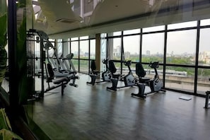 Un gimnasio con equipo de ejercicio, amplias ventanas y vista a un paisaje urbano.