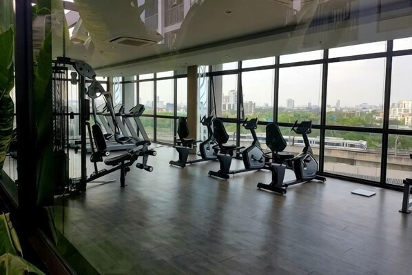 Een sportschool met trainingsapparatuur, grote ramen en uitzicht op een stadsbeeld.