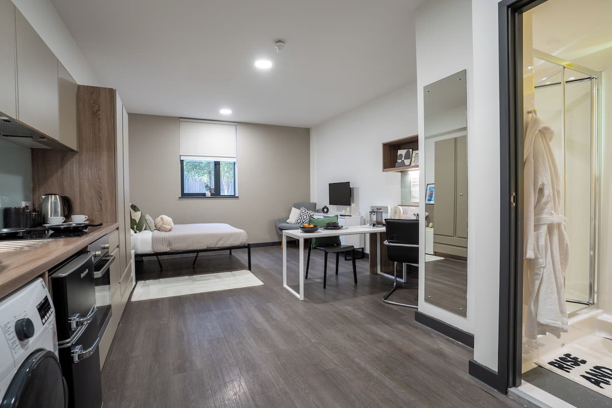 Une chambre d’hôtel moderne équipée d’une kitchenette, d’un lit, d’un bureau et d’une salle de bain avec une douche en verre.