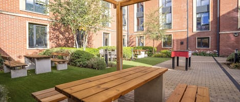 An outdoor patio area with picnic tables and a brick building in the background.
