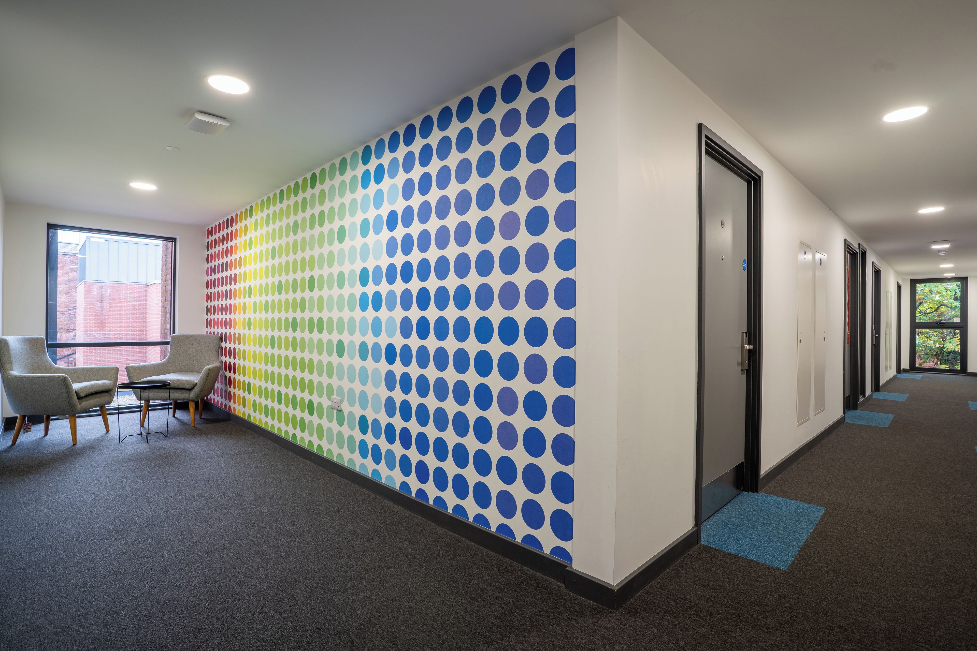 A modern office space with a patterned wall, a seating area, and a hallway leading to doors.