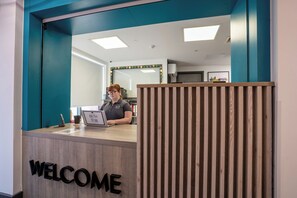 A reception desk with a 'WELCOME' sign, a laptop, and a framed certificate. - Student Only Sycamore House (Leeds)