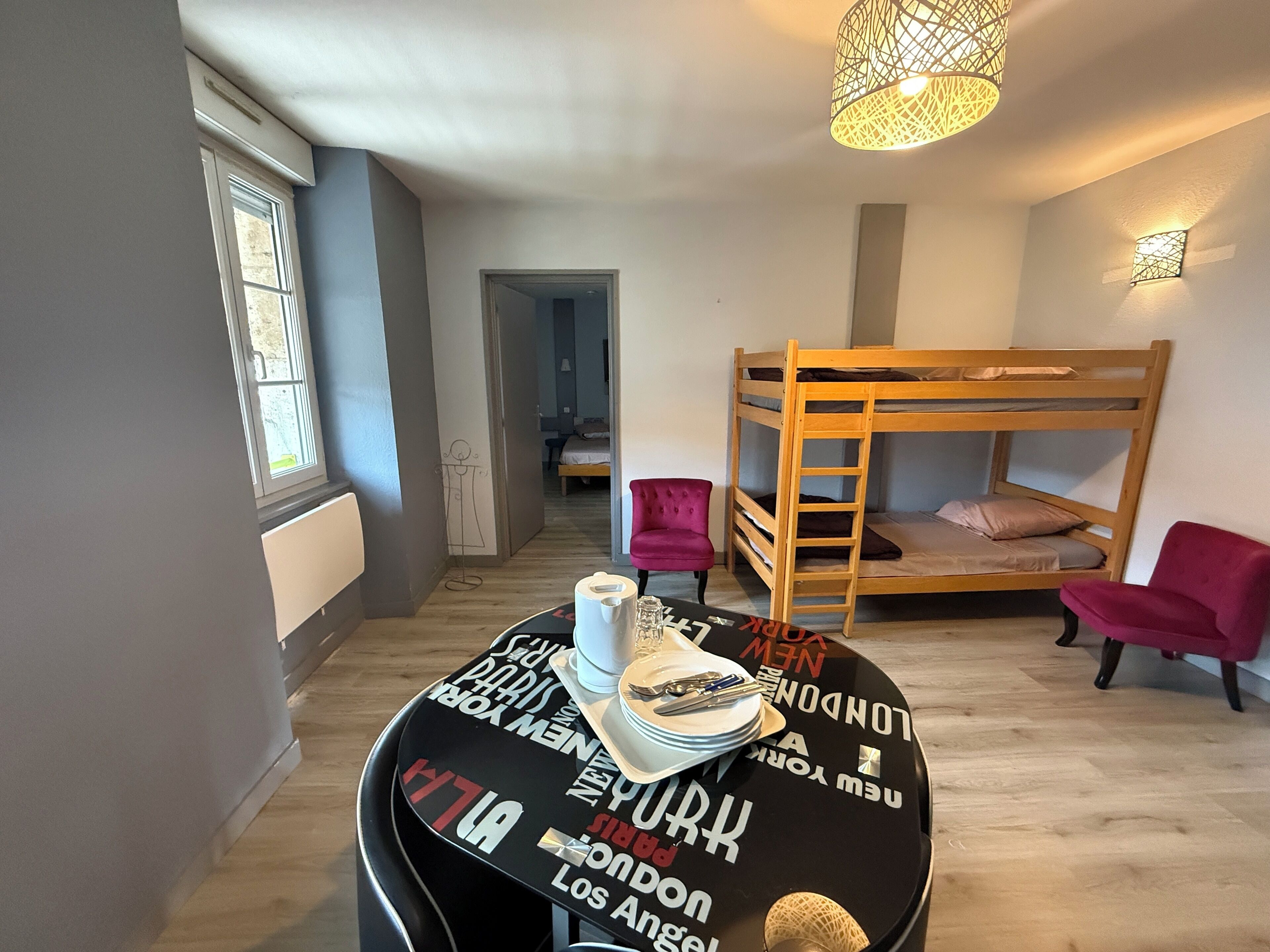 Een kamer met een stapelbed, een ronde tafel met een zwart oppervlak, en een hanglamp.