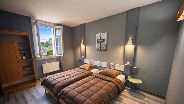 A bedroom with a bed, a wooden wardrobe, a radiator, a window with a view, and wall-mounted lights. - Hôtel de la Vallée (Ornans)