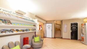 A hotel reception area with a reception desk, a staircase, and a waiting area with two armchairs. - Hôtel de la Vallée (Ornans)