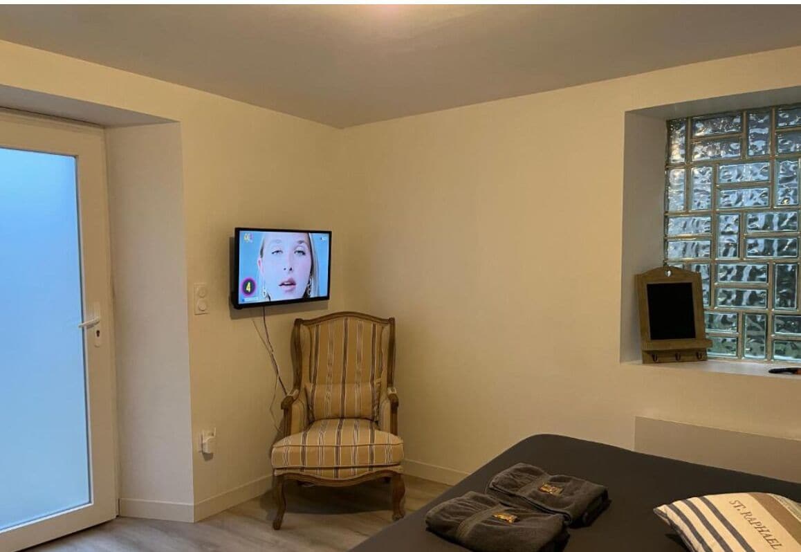 A room with a bed, a chair, a television mounted on the wall, and a window with a view of a building.