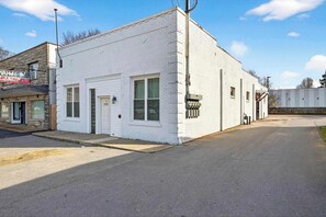 A white building with a garage door, a small window, and a utility meter on the side. - The Billy Walters Suite | Modern Brick Retreat! (Louisville)