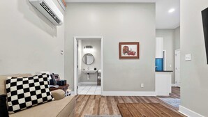 Ein Wohnzimmer mit einer Couch, einem karierten Zierkissen, einem Couchtisch, einem Teppich und einem Flur, der zu einem Badezimmer führt.