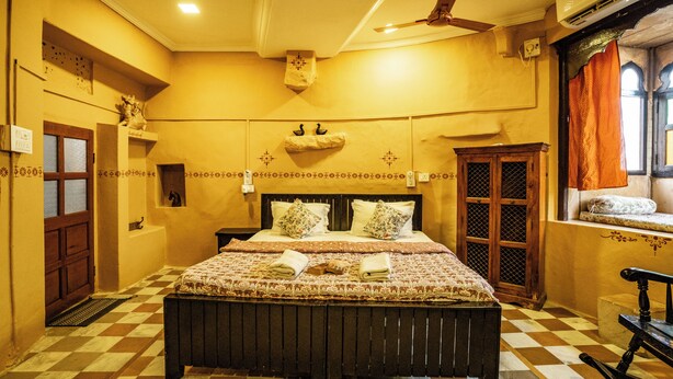 Una habitación con piso a cuadros, una cama con ropa de cama estampada, un cabecero de madera, un ventilador de techo y una ventana con cortinas.