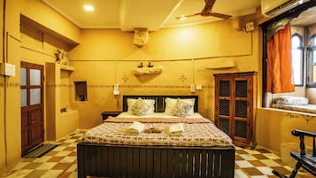 A room with a checkered floor, a bed with patterned bedding, a wooden headboard, a ceiling fan, and a window with curtains.