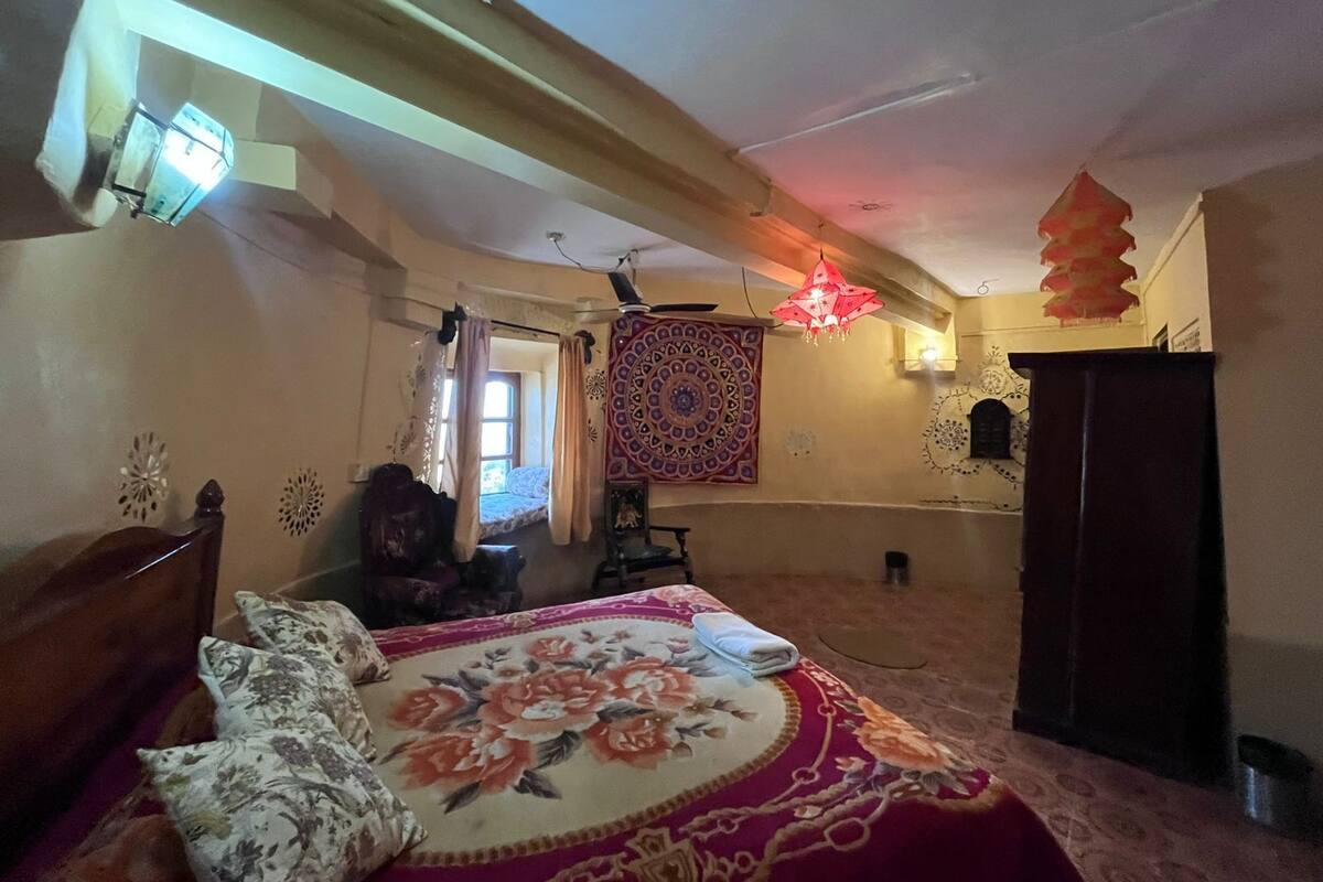 A bedroom with a bed, a wardrobe, a tapestry, and a hanging light fixture.