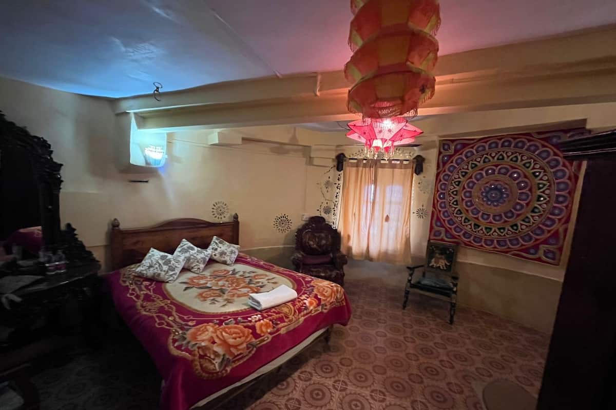 A bedroom with a bed, a wooden headboard, a chandelier, a tapestry, and a mirror.
