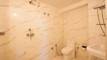 A bathroom with marble walls, a toilet, a sink, and a shower.