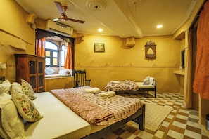 Une chambre traditionnelle comprenant un lit, une chaise, une fenêtre avec des rideaux, un ventilateur de plafond et un climatiseur fixé au mur.