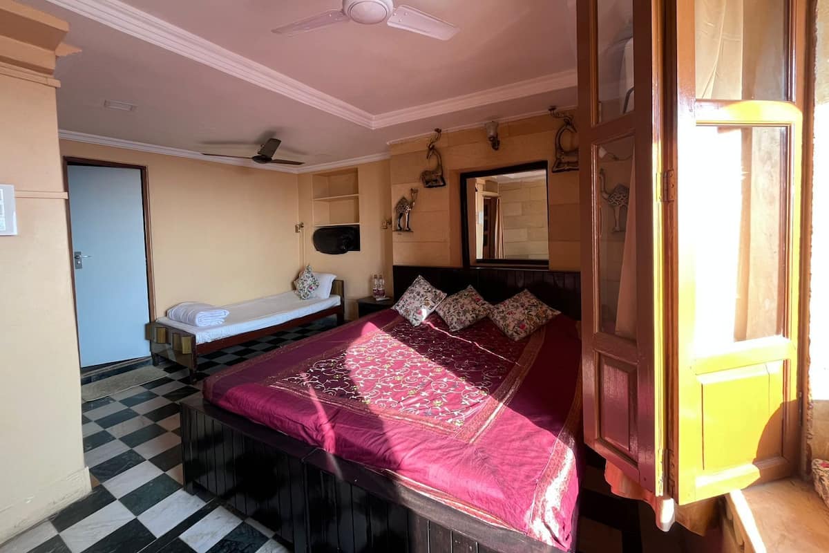 A room with a bed, a small bedside table, a ceiling fan, a mirror, and a checkered floor.
